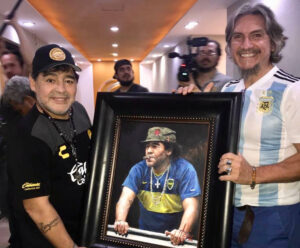 Diego Maradona standing next to portrait by Fabian Perez