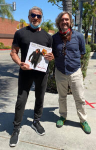 Sylvester Stallone holding art book next to Fabian Perez